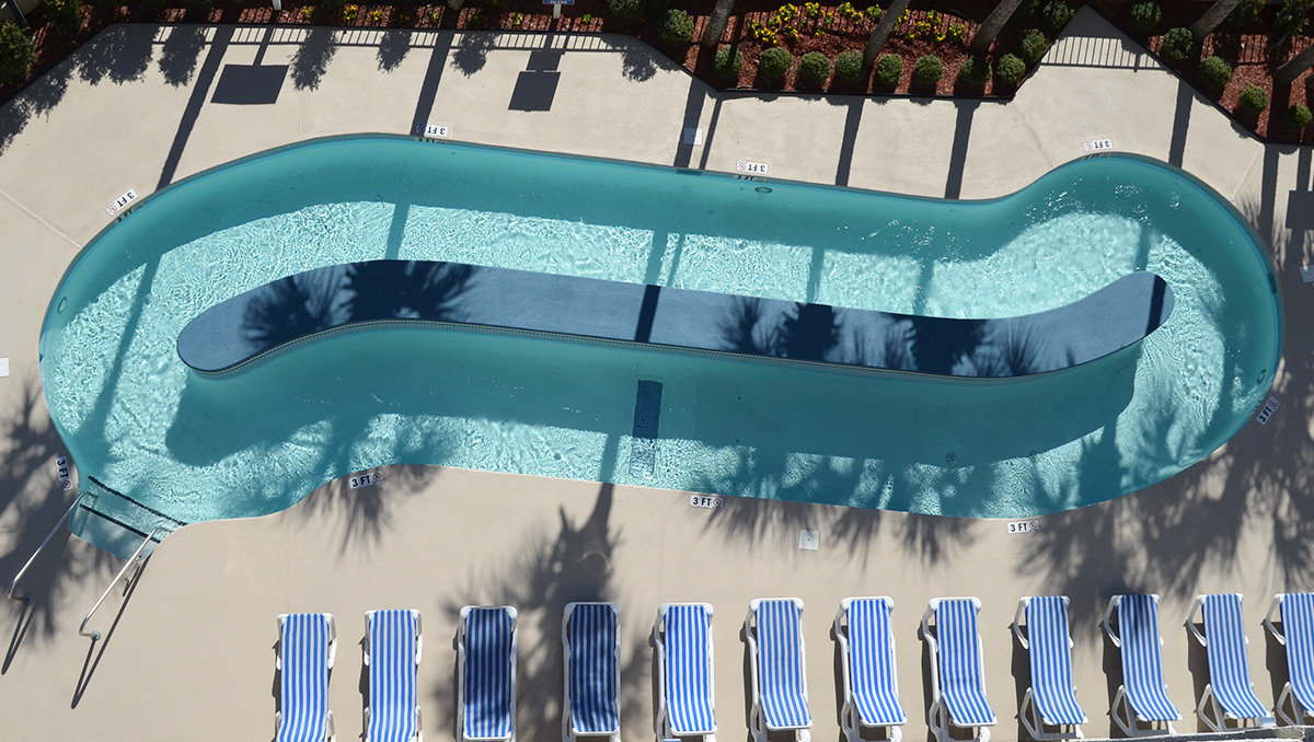 An aerial view of a swimming pool with blue and white lounge chairs arranged around it.