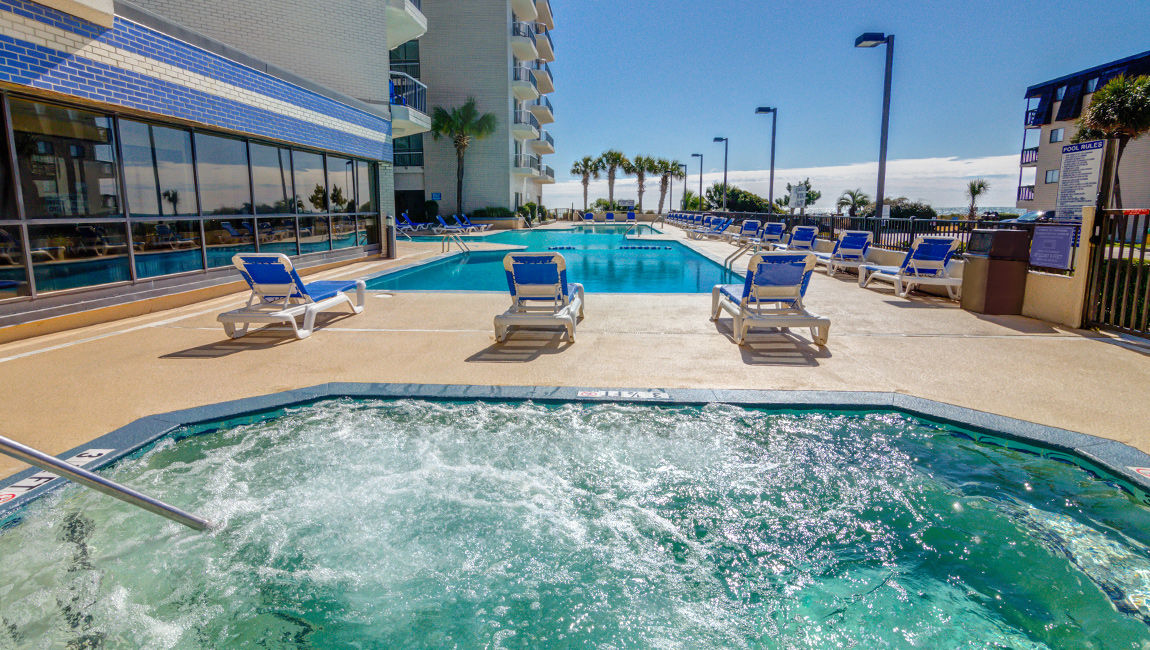 A pool area with a hot tub, lounge chairs, and a building in the background.