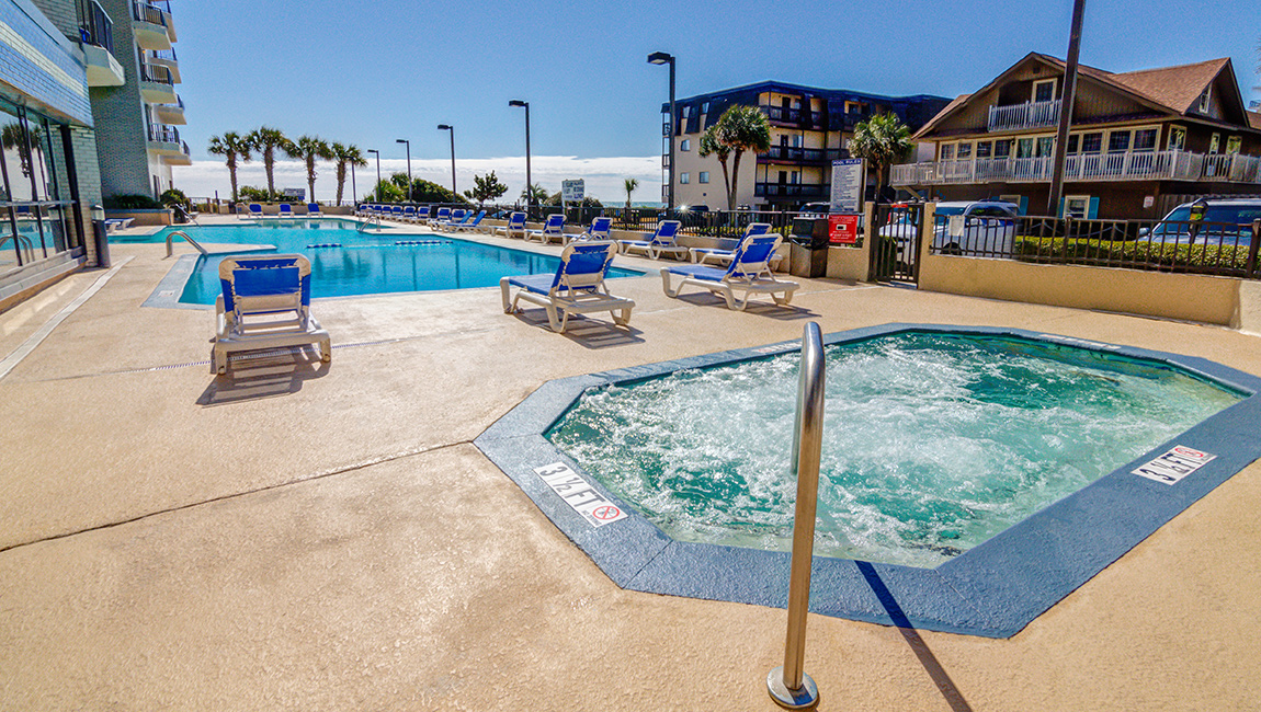 A swimming pool and hot tub surrounded by lounge chairs and buildings.