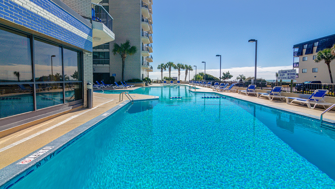 A large outdoor pool with lounge chairs and palm trees in the background