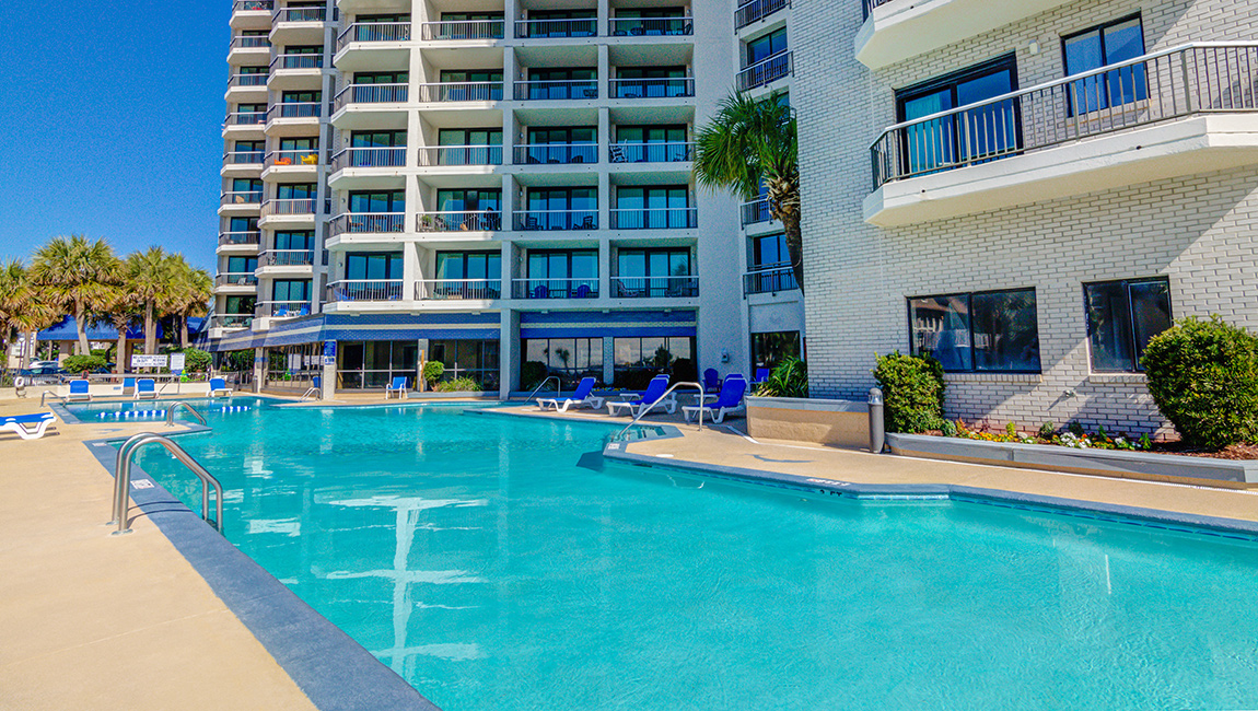 A large pool with blue lounge chairs and a tall building in the background