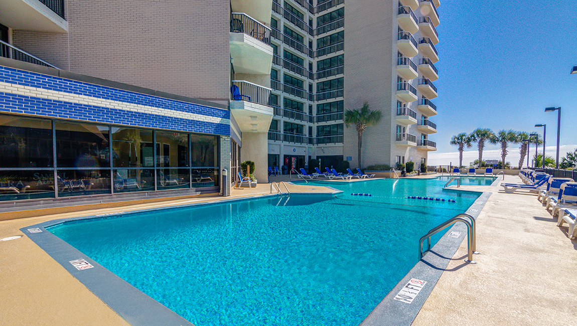 A large swimming pool with a building and balconies in the background.